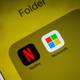 A phone with the word folder at the top of the screen holding both the Netflix and Microsoft app icons.
